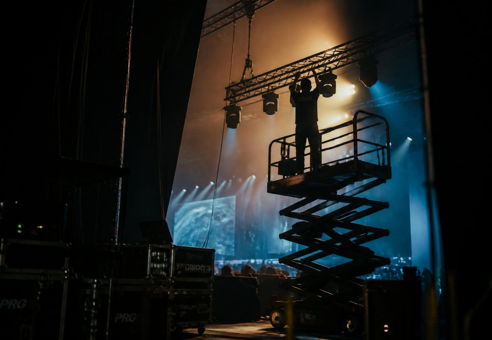 Stagehand on a scissor lift rigging moving lights on a truss above a concert stage